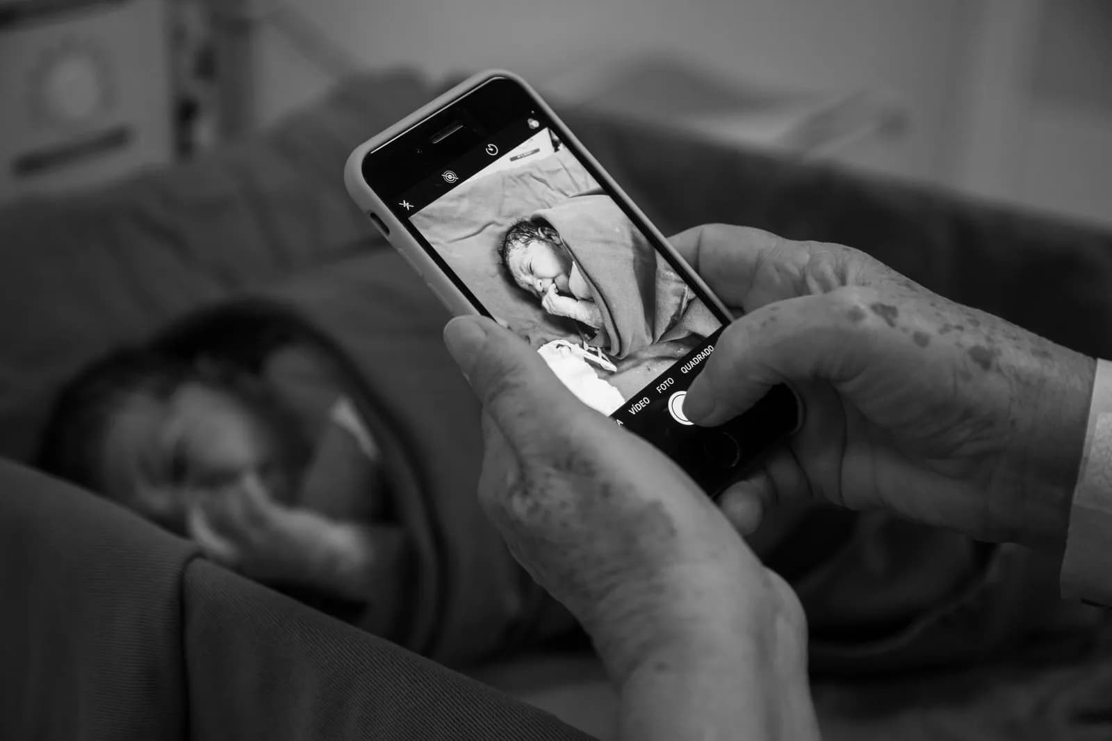 Een opa of oma fotografeert een slapende pasgeborene met een telefoon